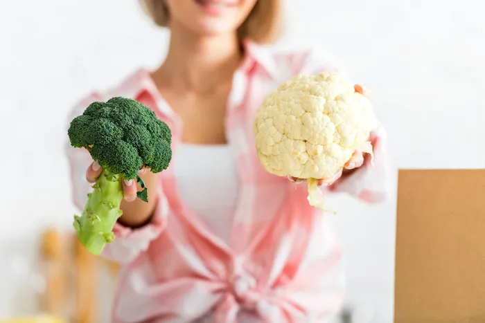 Woman holding up a head of broccoli and a head of cauliflower | 7 Tips to Lower Uric Acid