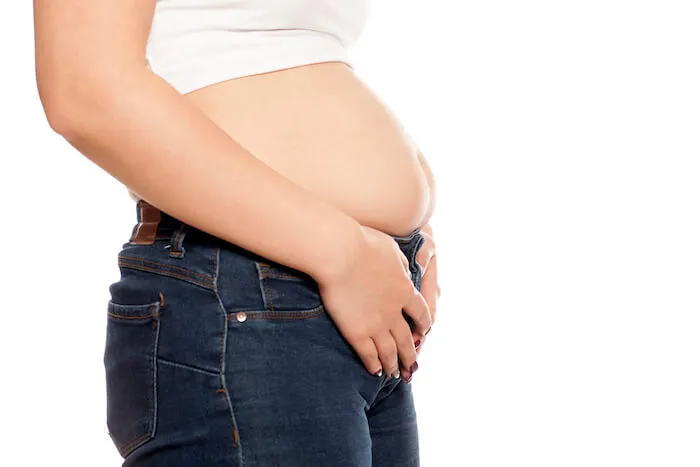 Woman in a white shirt and jeans showing her bloated stomach | Abdominal Gas and Bloating? Do This Now!