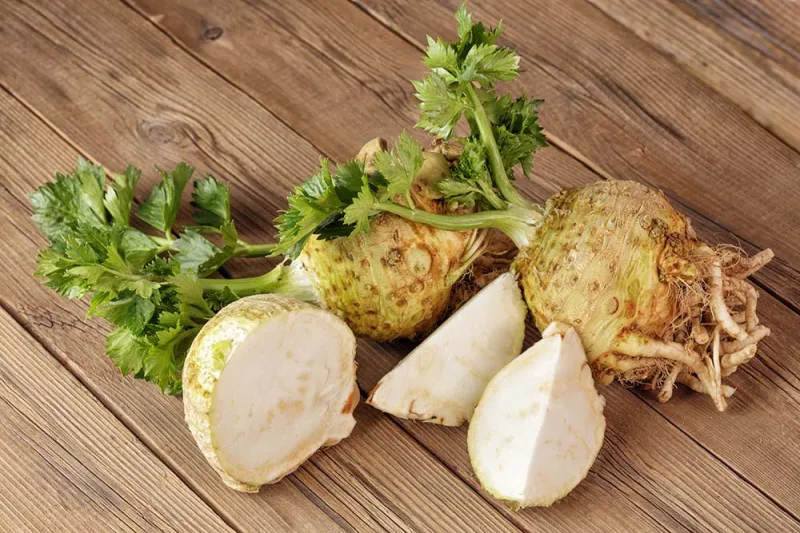 Whole and cut celeriac root on wooden table