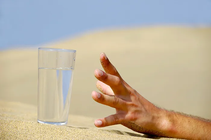 Hand reaching for water on hot desert sand