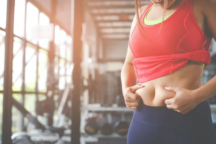 Woman in workout clothes pinching stomach fat | What is Your Body Type?