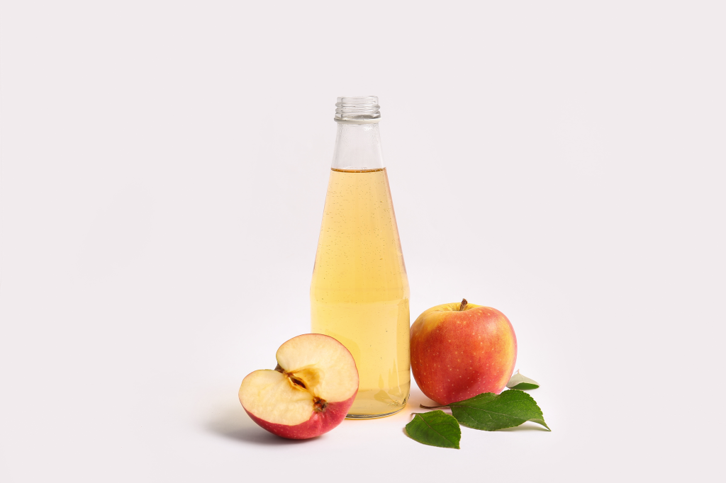 bottle of apple cider vinegar next to a half of an apple