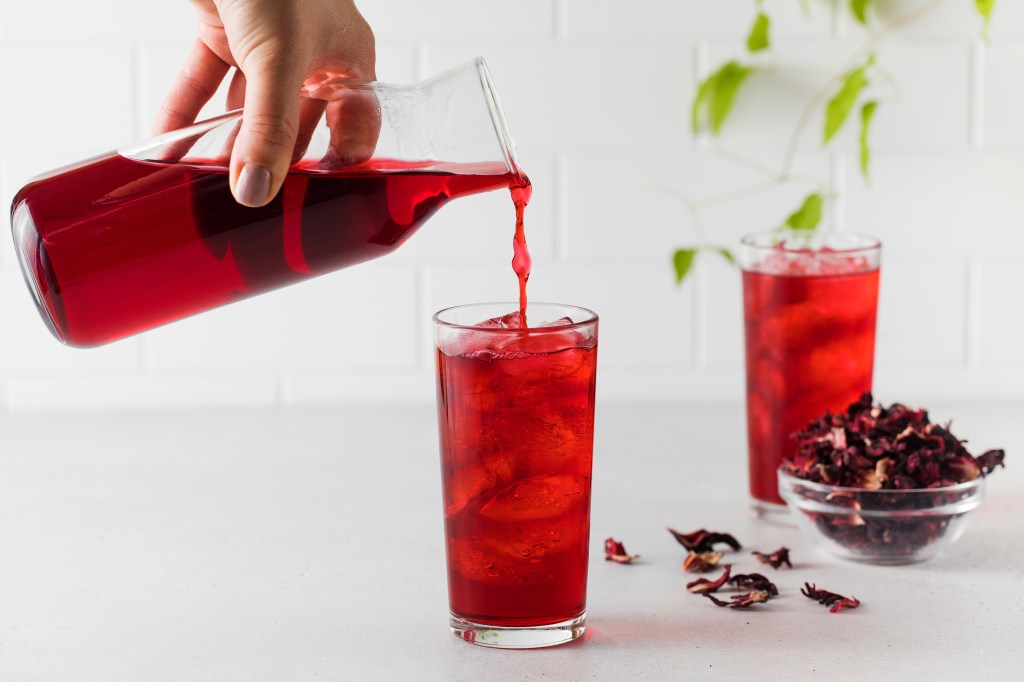 a person pouring hibiscus drink into a glass