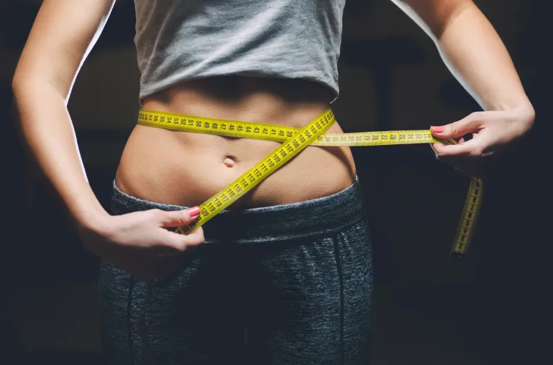 Woman measuring waist with yellow tape measure