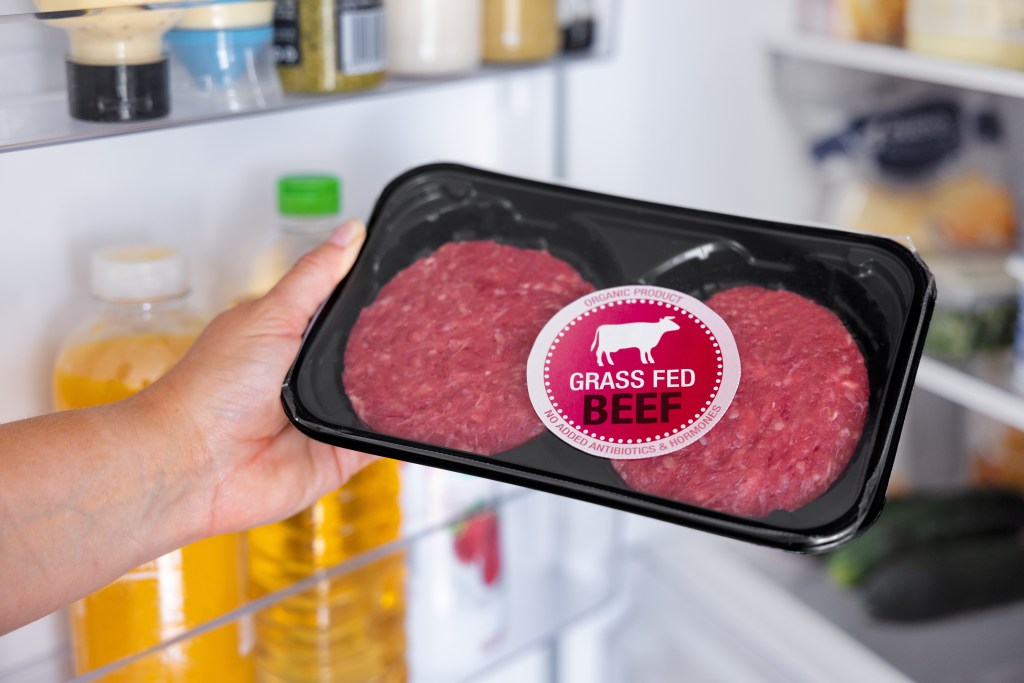 a hand holding a tray of grass-fed meat