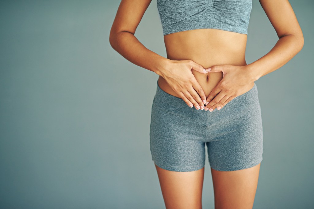 Woman in shorts and top with her hands on her stomach