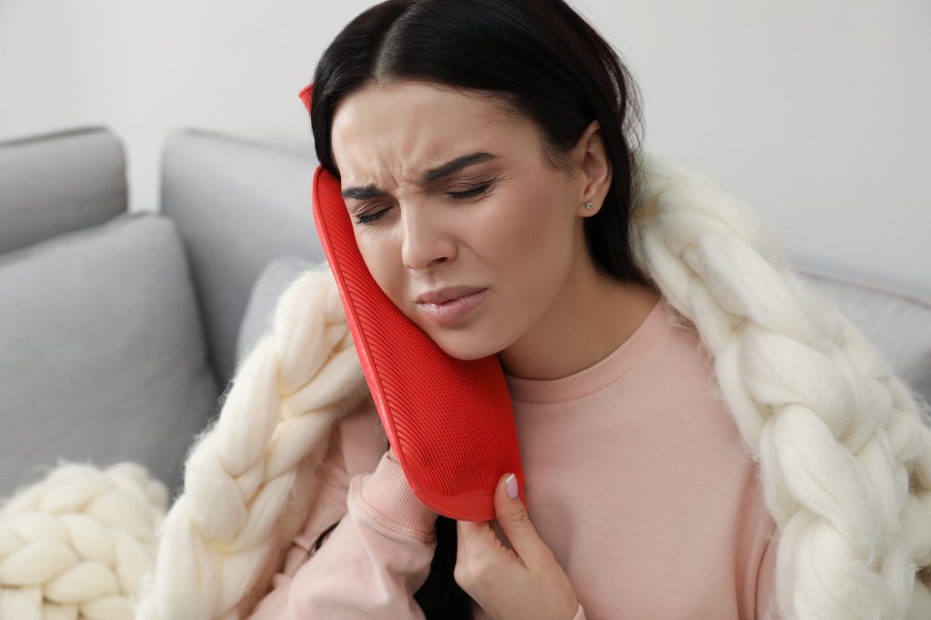 woman using a heat pack on her ear for pain relief ear infection home remedy