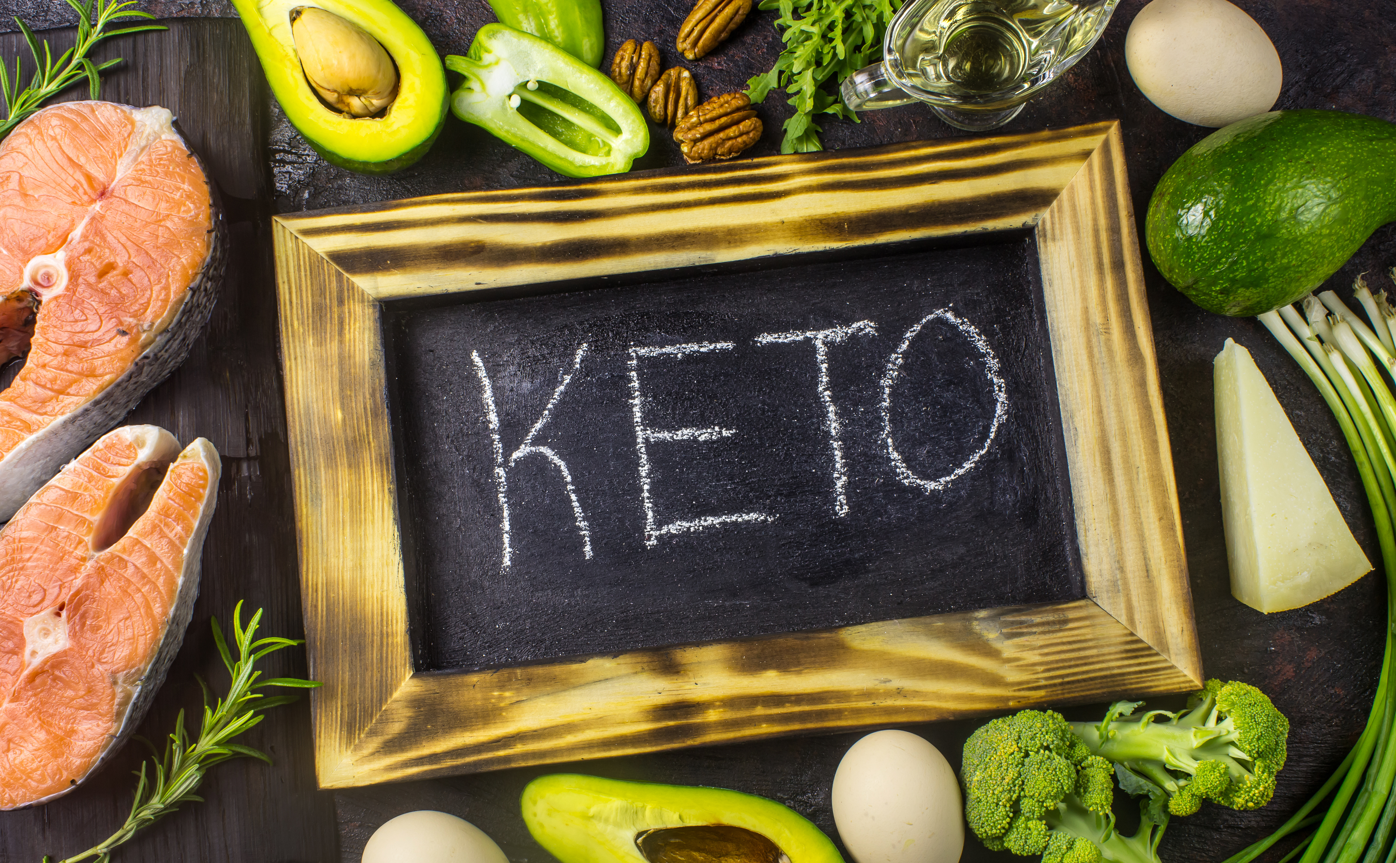Keto diet foods including avocado, eggs, salmon, nuts, cheese and leafy green vegetables arranged on a table