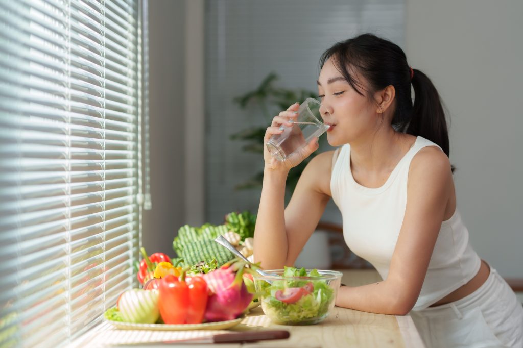 Woman drinking water next to a bowl of salad 