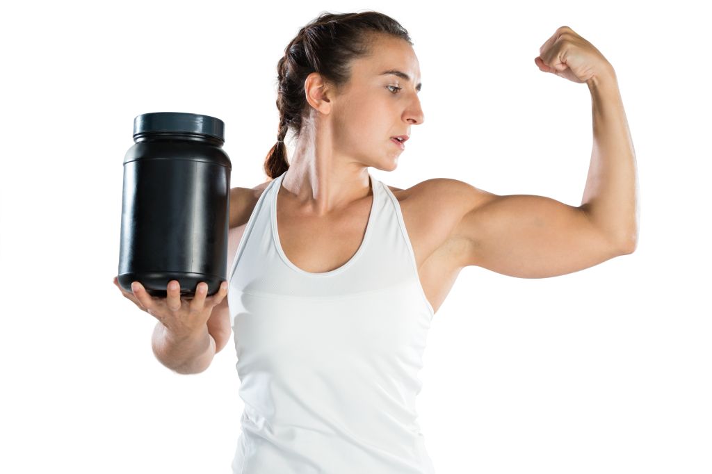 Woman flexing muscles while holding a supplement bottle 